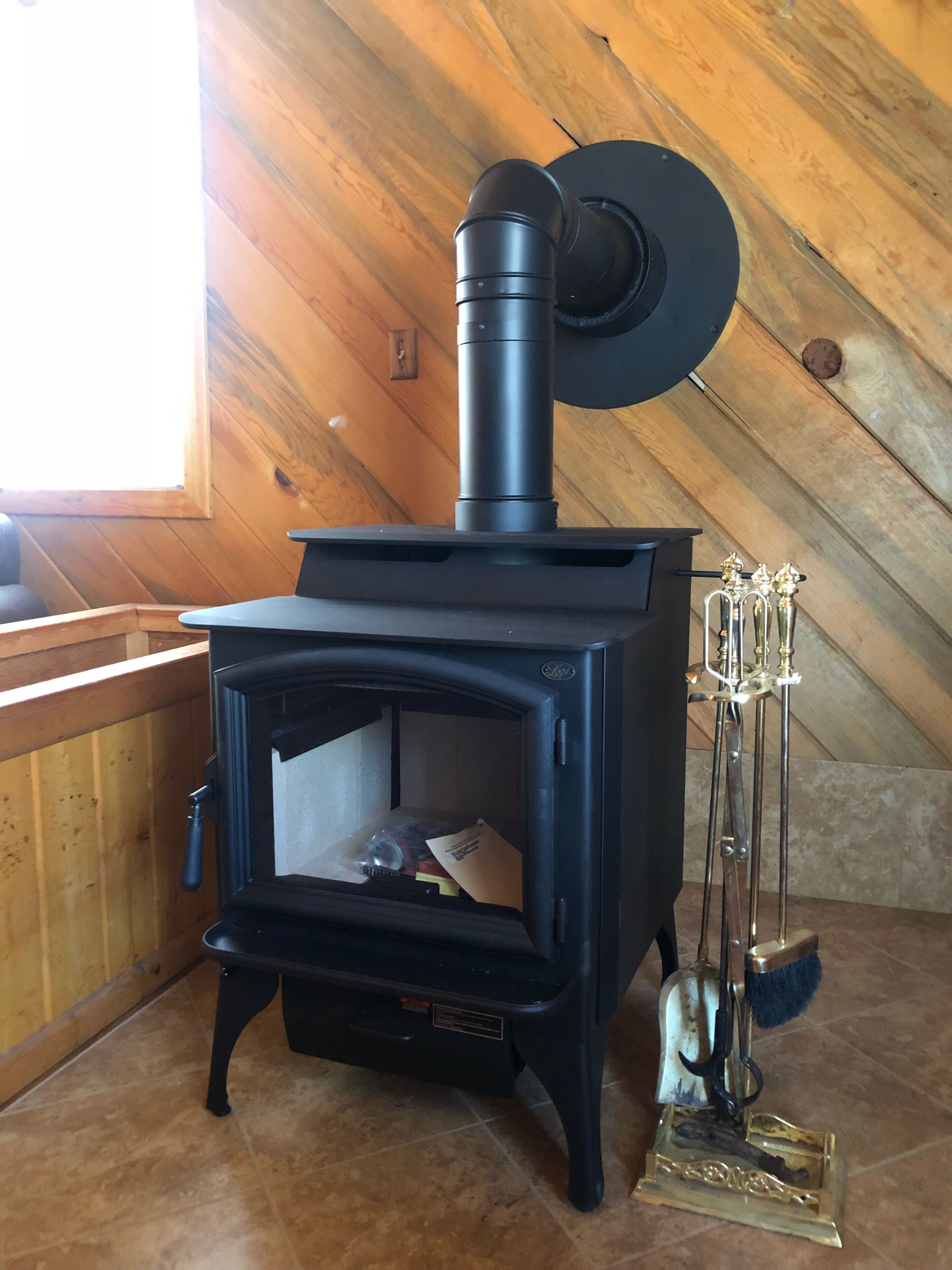 A wood-burning stove in a room with wooden walls and a sloped ceiling.