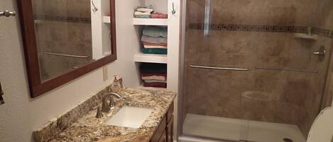 A bathroom with a granite countertop sink, a mirror, a shower enclosure, and a toilet.