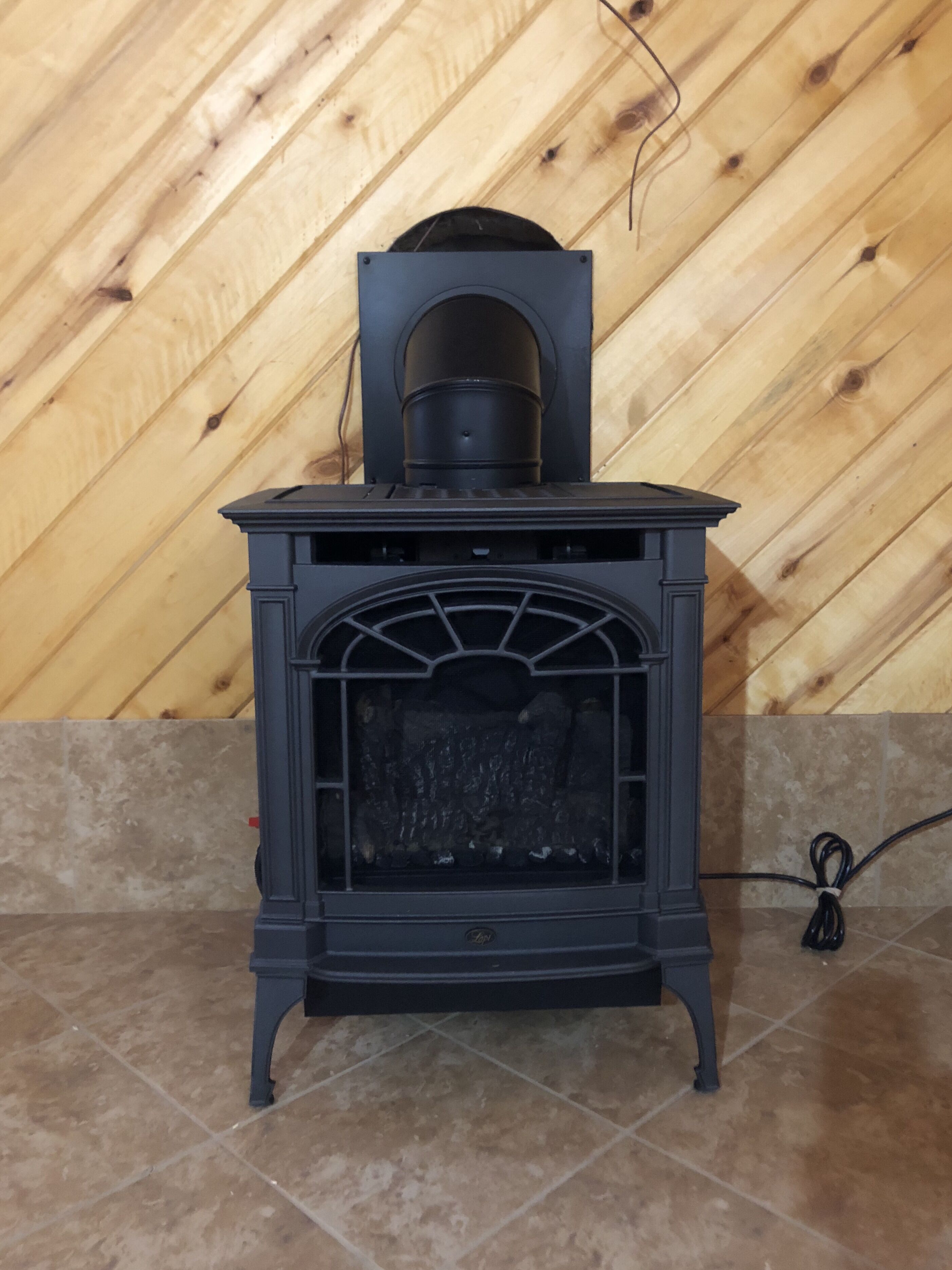 A black wood-burning stove with a chimney, set against a wooden wall and tiled floor.