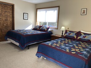 Een slaapkamer met twee bedden, elk voorzien van een blauwe quilt met een hertenprint, een raam met zonwering en een houten deur.