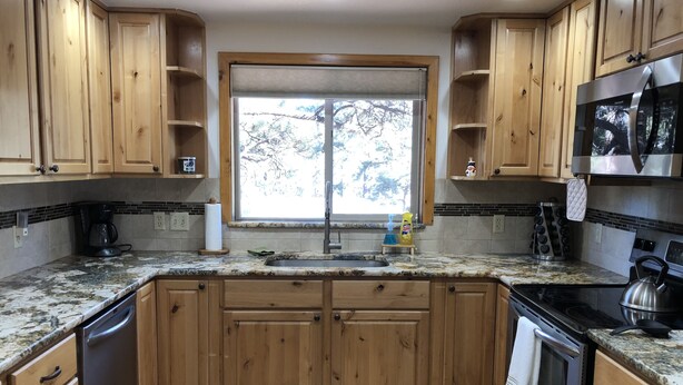 Eine Küche mit Holzschränken, einem Edelstahlkühlschrank, einem Herd und einem Fenster mit Blick auf Bäume.