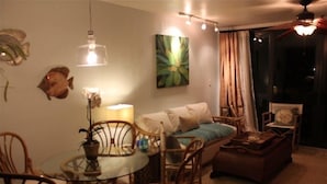A cozy living room with a glass dining table, wicker chairs, a sofa with cushions, a coffee table, and a large window with curtains. - Sapphire Beach is just a few steps out your door!!! (St. Thomas)