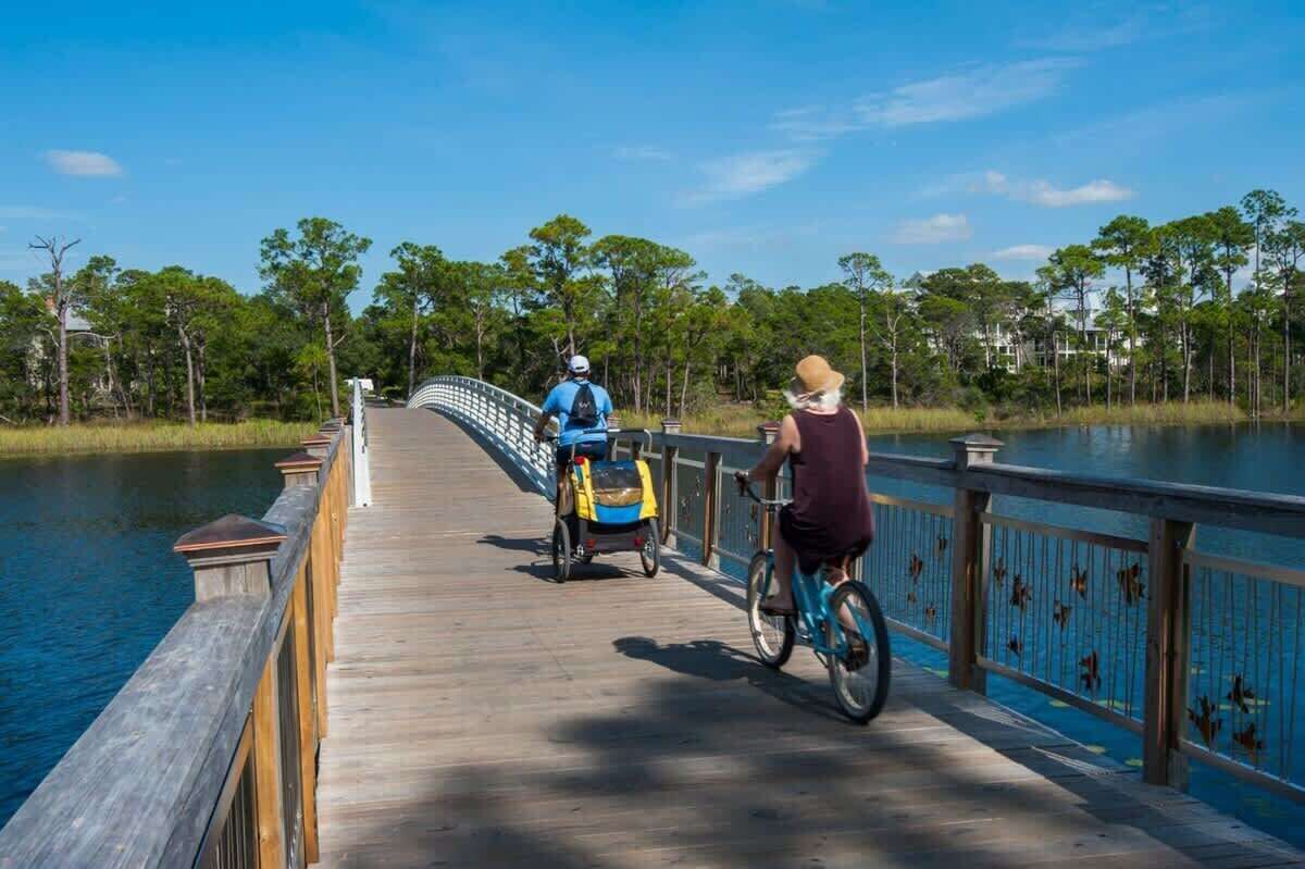 A wooden boardwalk over water with people riding bicycles and a stroller.