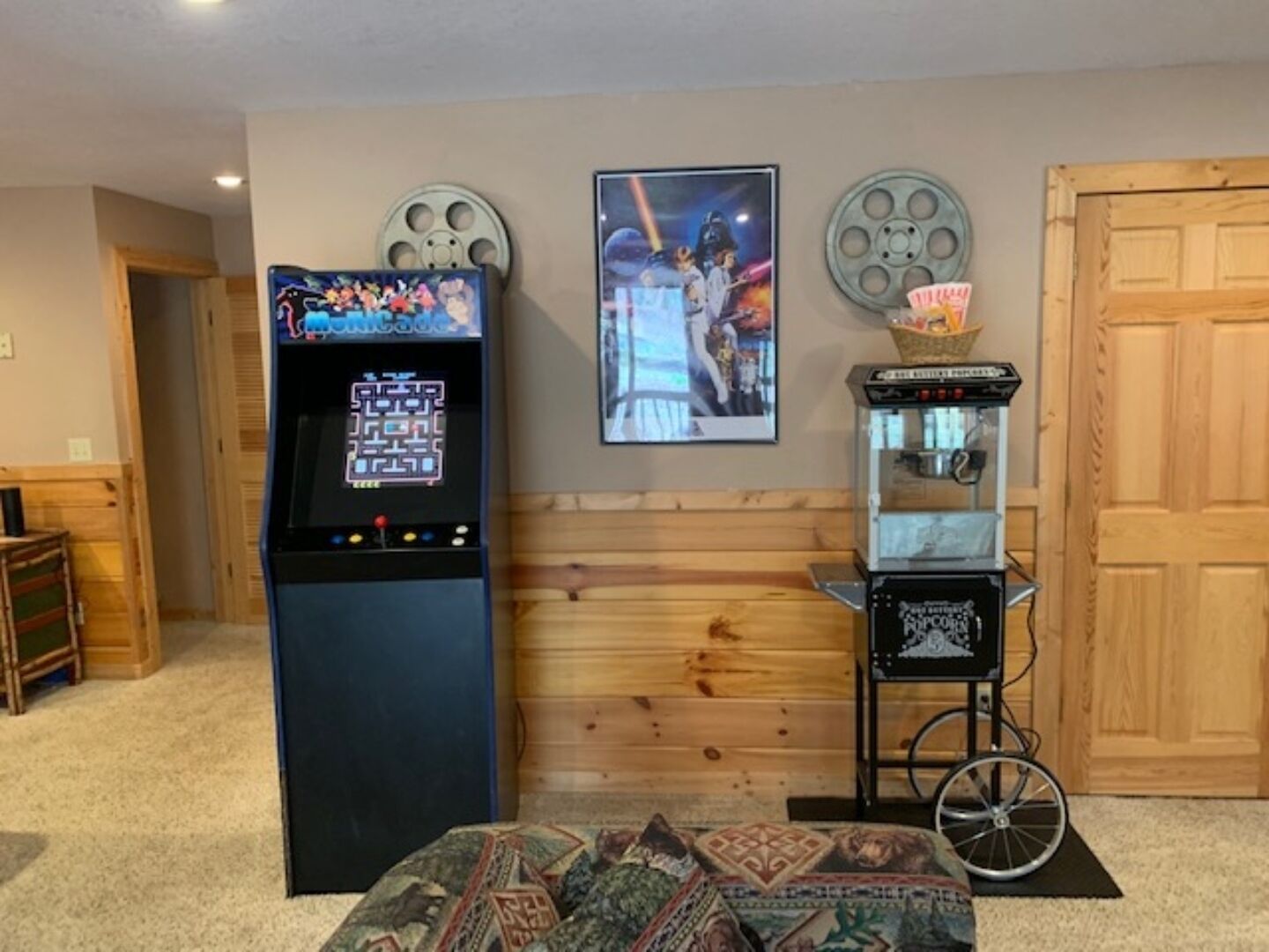 A room with a retro arcade machine, a framed movie poster, a popcorn machine, and a wooden bench.