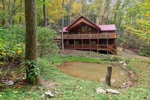 Une cabane dotée d’un balcon, entourée d’une forêt et bordée d’un étang.