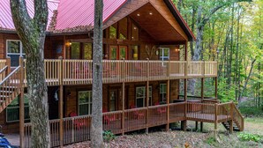 A two-story log cabin with a red roof, multiple decks, and a staircase leading to the upper level. - Large, Spacious, Relaxing 4 Bedroom 4.5 Bath Pigeon Forge Tennessee Cabin (Sevierville)