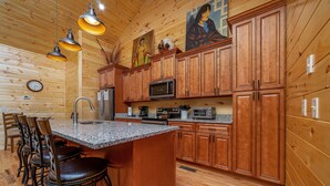 A wooden cabin interior with a kitchen featuring granite countertops, wooden cabinets, and a central island with bar stools. - Large, Spacious, Relaxing 4 Bedroom 4.5 Bath Pigeon Forge Tennessee Cabin (Sevierville)