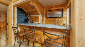 A wooden interior with a kitchen area, a stone fireplace, and a bar with stools. - Large, Spacious, Relaxing 4 Bedroom 4.5 Bath Pigeon Forge Tennessee Cabin (Sevierville)