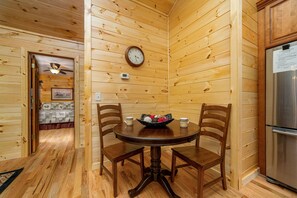 Un intérieur en bois avec une table de salle à manger ronde, quatre chaises, une horloge et un réfrigérateur.