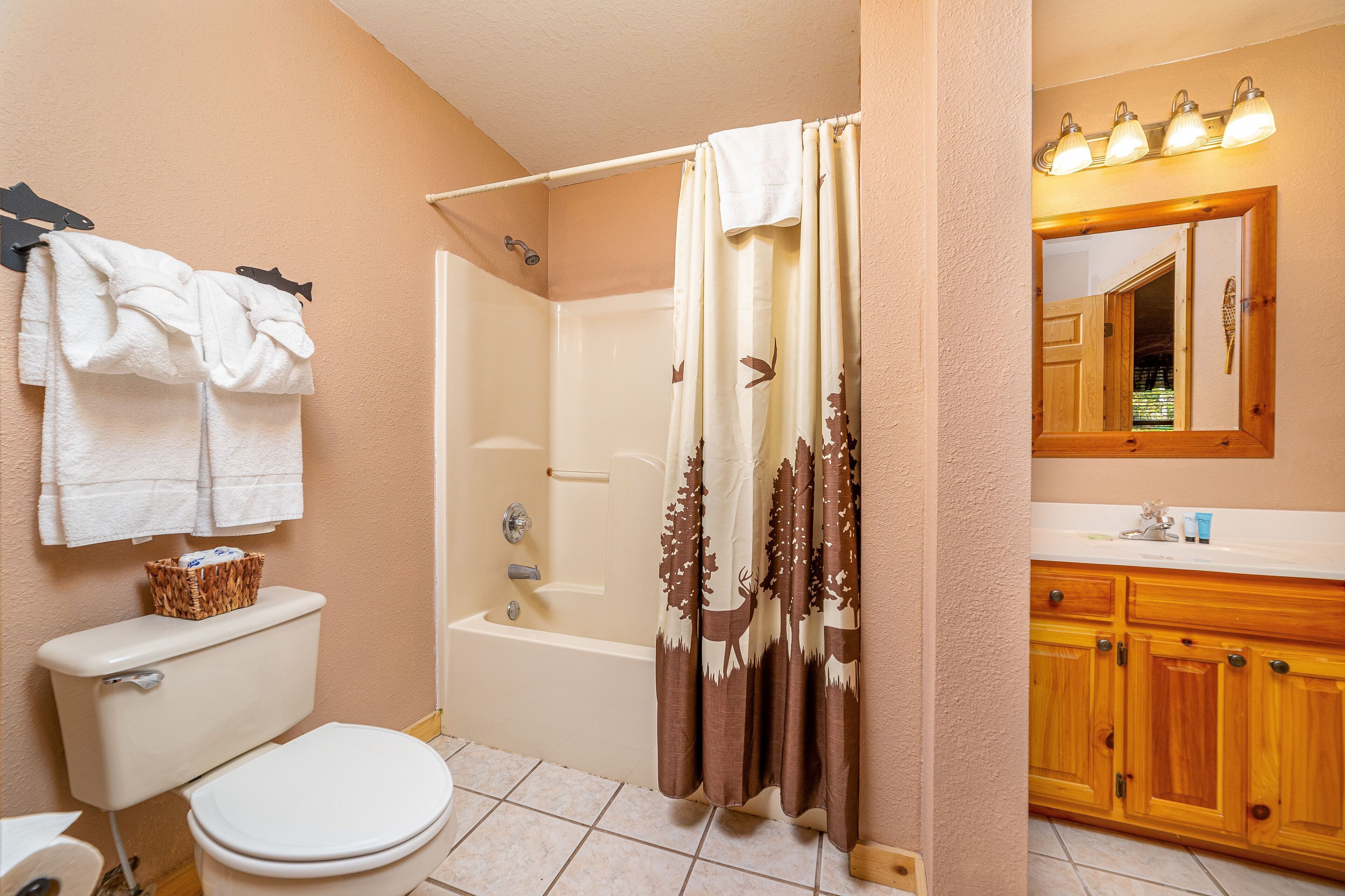 A bathroom with a toilet, bathtub, shower curtain, and wooden cabinets.