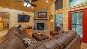 A cozy log cabin interior with a fireplace, leather sofas, a flat-screen TV, and a ceiling fan. - Large, Spacious, Relaxing 4 Bedroom 4.5 Bath Pigeon Forge Tennessee Cabin (Sevierville)