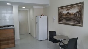 A kitchen with a refrigerator, a dining table with chairs, and a painting on the wall. - Apartamento Estudio na Pitangueiras (Guarujá)