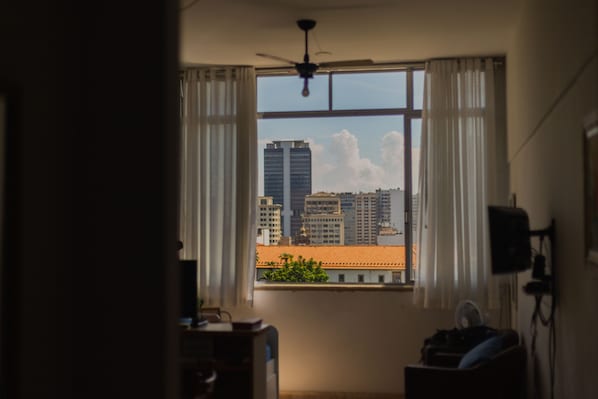 A room with a large window, a ceiling fan, and a view of a cityscape.