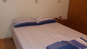 Una cama individual con una manta y almohadas a rayas, una mesita de noche de madera con una botella y un armario de madera.