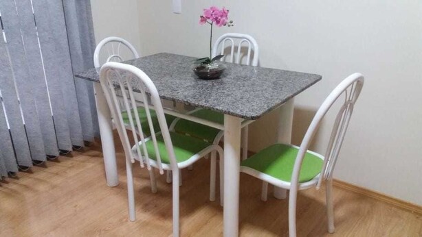 Una mesa de comedor con cuatro sillas blancas, cada una con un cojín verde. Un jarrón con una flor rosa está sobre la mesa.