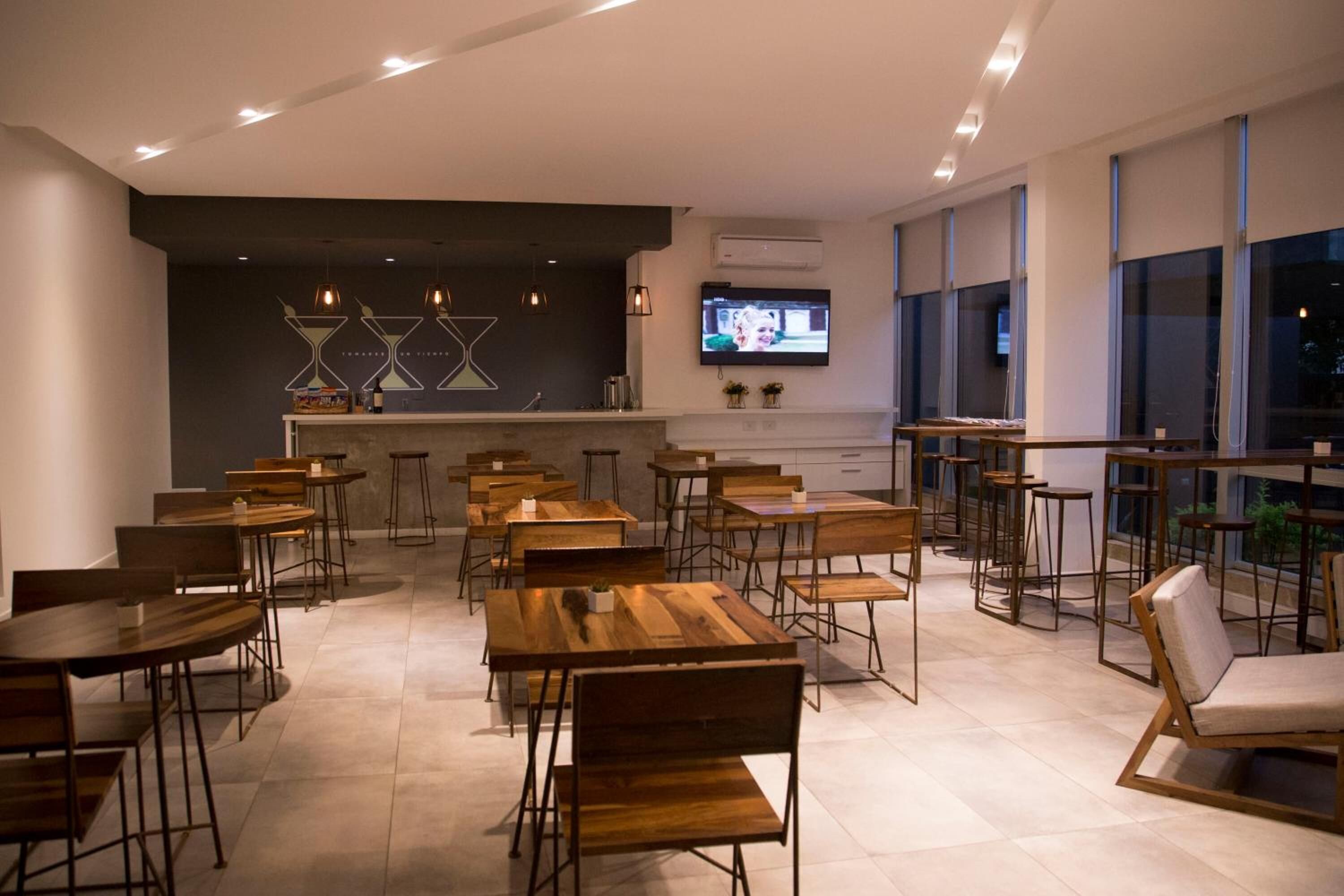 A modern dining area with wooden tables and chairs, a bar area with stools, and a television mounted on the wall.
