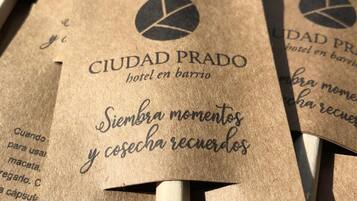 Una serie de bolsas de papel marrón con el texto "CIUDAD PRADO hotel en barrio" y "Siembra momentos y cosecha recuerdos".