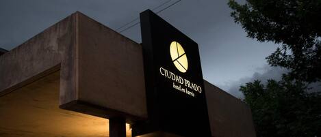 A hotel sign with a modern design, featuring a logo and the name 'CIUDAD PRADO hotel en barrio'.
