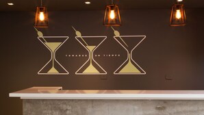 A bar area with a white counter and three stools. Above the counter, there are three hourglass-shaped light fixtures with a warm glow. - Ciudad Prado Hotel (Córdoba)