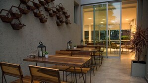 An outdoor dining area with wooden tables and chairs, potted plants, and hanging baskets on the wall. - Ciudad Prado Hotel (Córdoba)