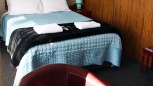 Un llit de matrimoni amb un edredó blau i negre, almoines blanques i una petita taula de nit amb una làmpada.