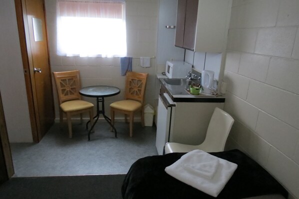 A small, compact room with a bed, a table with two chairs, a sink, and a window with curtains.