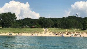 Ein Strand mit sandigem Ufer, einer Wasserfläche im Vordergrund und einer bewaldeten Hügelkette im Hintergrund.