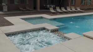 A swimming pool with a hot tub section, lounge chairs, and a building in the background. - 6 Minutes from Airport, 8 Minutes to Strip,  Sleeps 14  6 Bedroom, 4 Bath (Las Vegas)