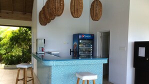 A kitchen with a blue tiled island, wooden stools, a coffee machine, a refrigerator, and a Pepsi refrigerator. - Your Secret Paradise , Richmond-St.Ann (St.Anns)