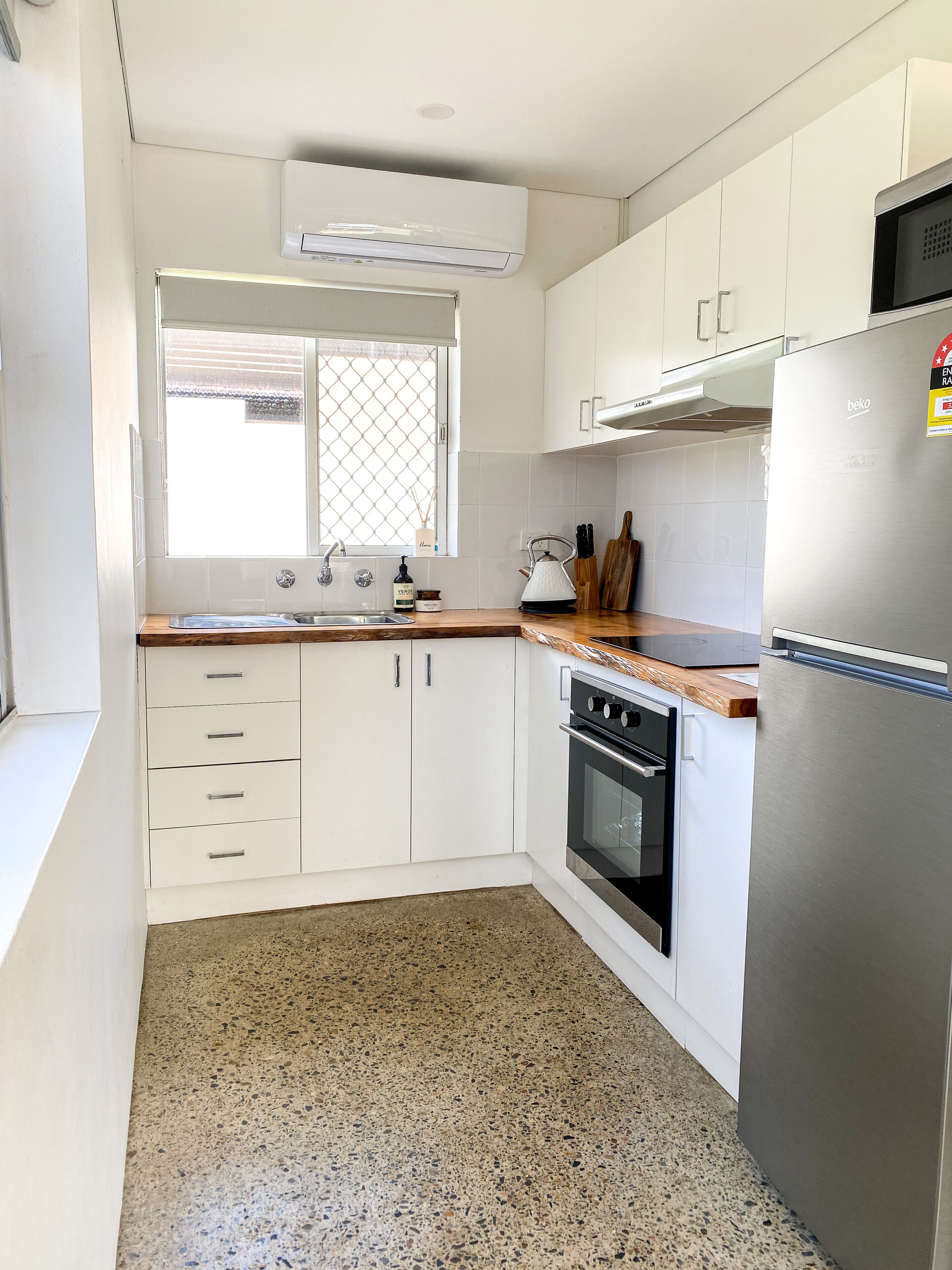 Una cuina moderna amb armaris blancs, un refrigerador d'acer inoxidable, un forn integrat i una finestra amb vistes.