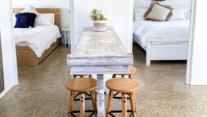 Un tavolo in legno rustico con quattro sgabelli in una stanza dal pavimento screziato, un letto con biancheria bianca e uno specchio appeso al muro.