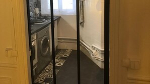 Une cuisine équipée d’un lave-linge, une fenêtre avec des rideaux et une horloge au mur.