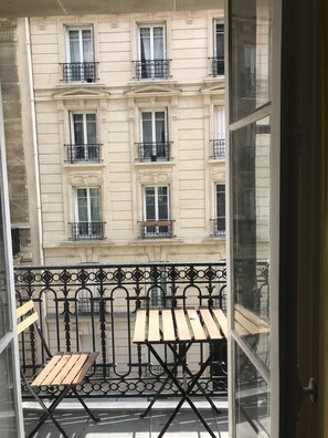A balcony with a wooden table and chairs, a wrought iron railing, and a view of a building with multiple windows and balconies. - Large family 3 rooms apartment (60m2), next to metro Convention (Paris)
