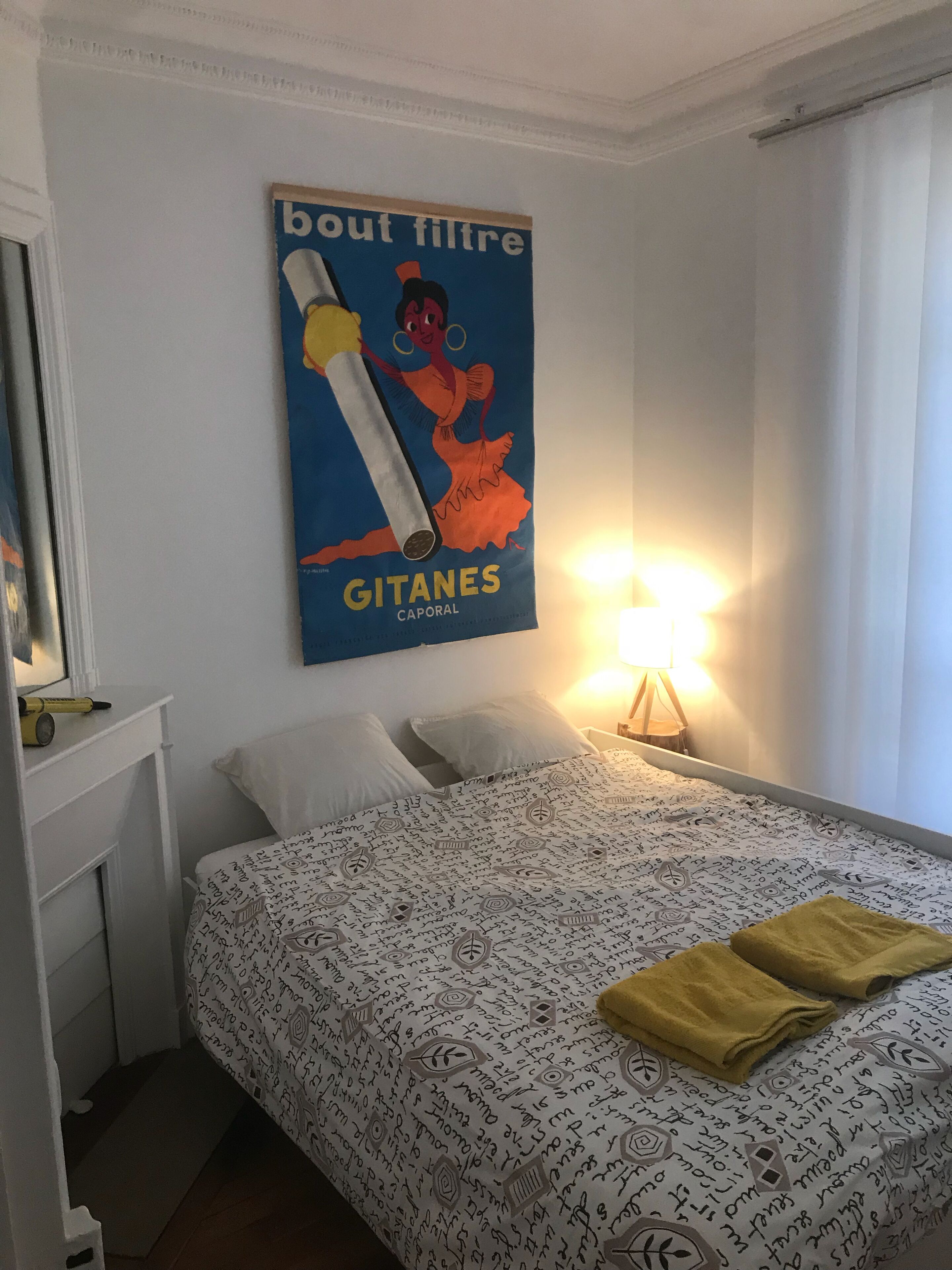 Une chambre d’hôtel avec un lit, des oreillers, une table de chevet avec une lampe et une affiche accrochée au mur.