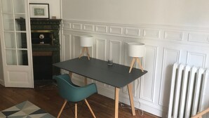 Une pièce avec une table en bois foncé, deux lampes blanches, une chaise de couleur turquoise et un radiateur blanc.