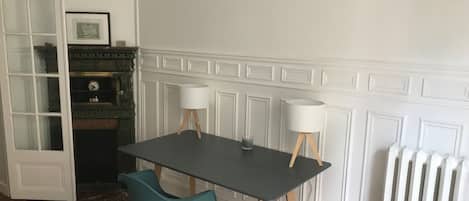 A room with a dark wooden table, two white lamps, a teal chair, and a white radiator.