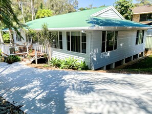 A single-story house with a green roof, a porch with chairs, and a small garden.