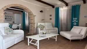 Un salon agrémenté d’une arche en pierre, de canapés blancs, d’une table basse blanche et de rideaux turquoise.