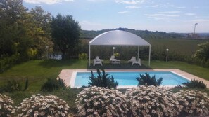 Una piscina con zona cubierta y sillas de descanso, rodeada por un jardín lleno de flores.