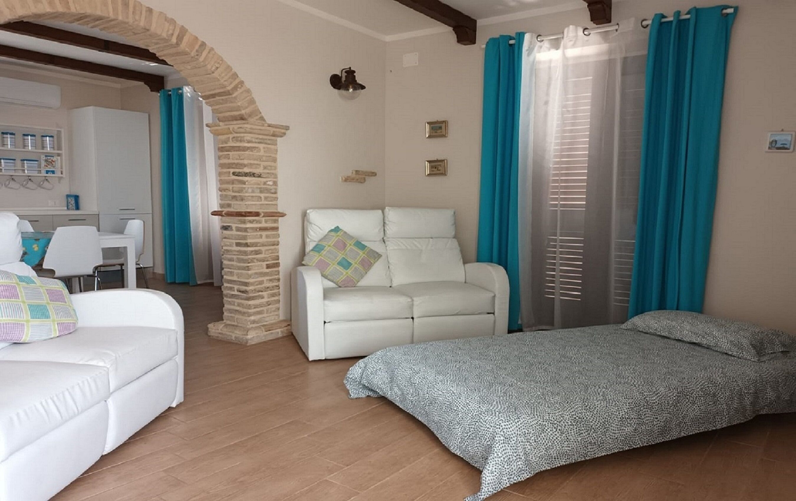Ein gemütliches Zimmer mit einer weißen Couch, einem geblümten Bett, einer Steinsäule und einem Fenster mit blauen Vorhängen.