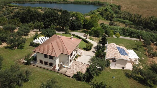 Une maison avec un toit recouvert de tuiles, un panneau solaire et un étang en arrière-plan.