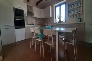 Una cocina con armarios blancos, horno empotrado y una mesa de comedor con sillas.