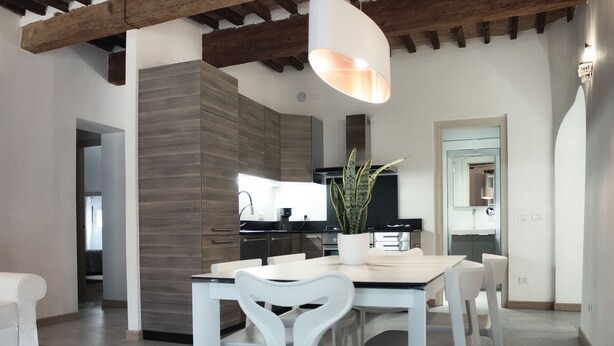 Une cuisine moderne dotée d’une cuisinière intégrée, d’un coin repas avec une table et des chaises blanches, et d’un luminaire suspendu.