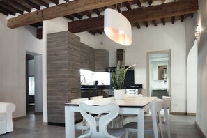 Una cocina moderna con estufa integrada, un comedor con mesa y sillas blancas, y una lámpara colgante.