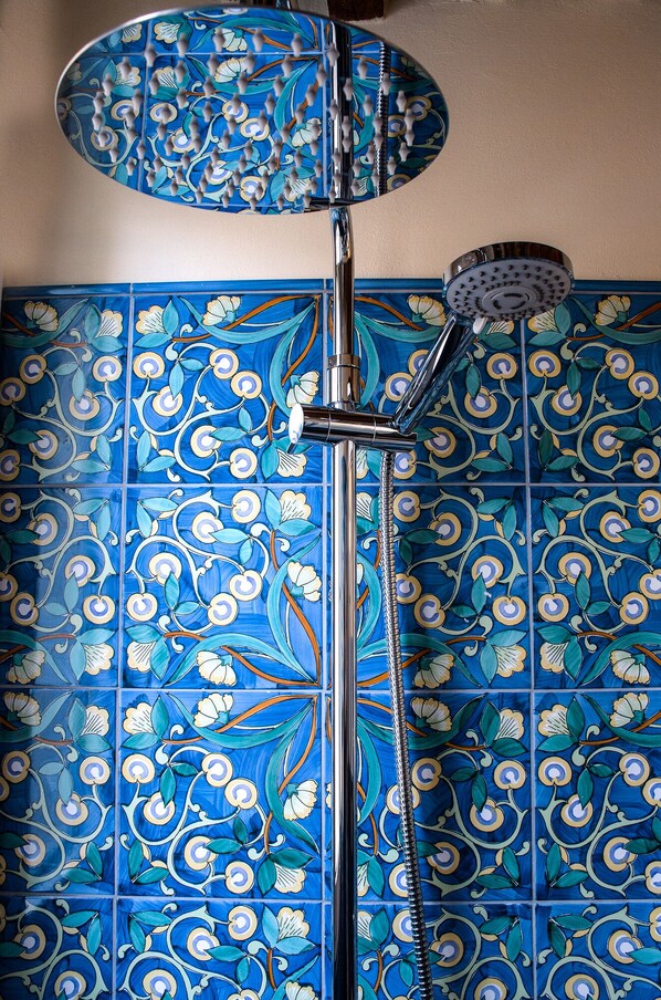 Un baño con azulejos florales azules, una ducha con cabezal de ducha manual y mampara de vidrio.
