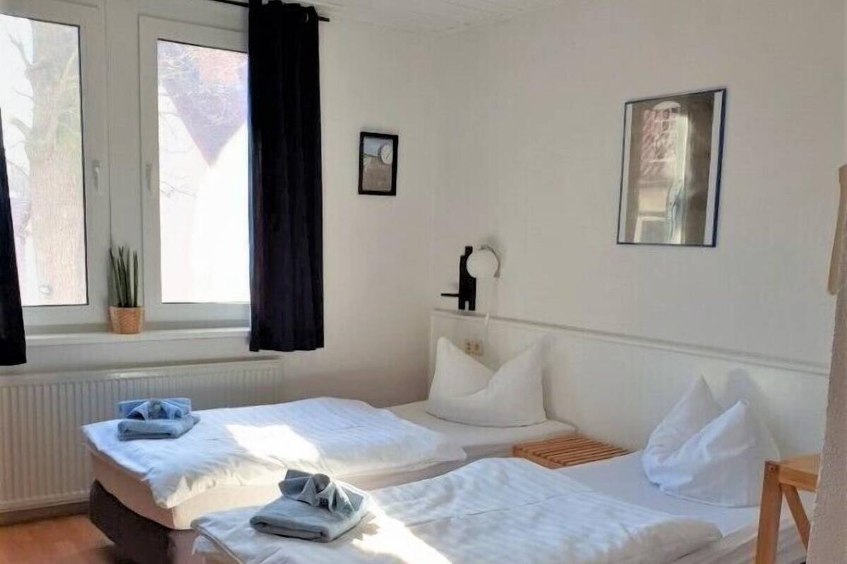 A room with two beds, a window with curtains, a radiator, and a ceiling light.