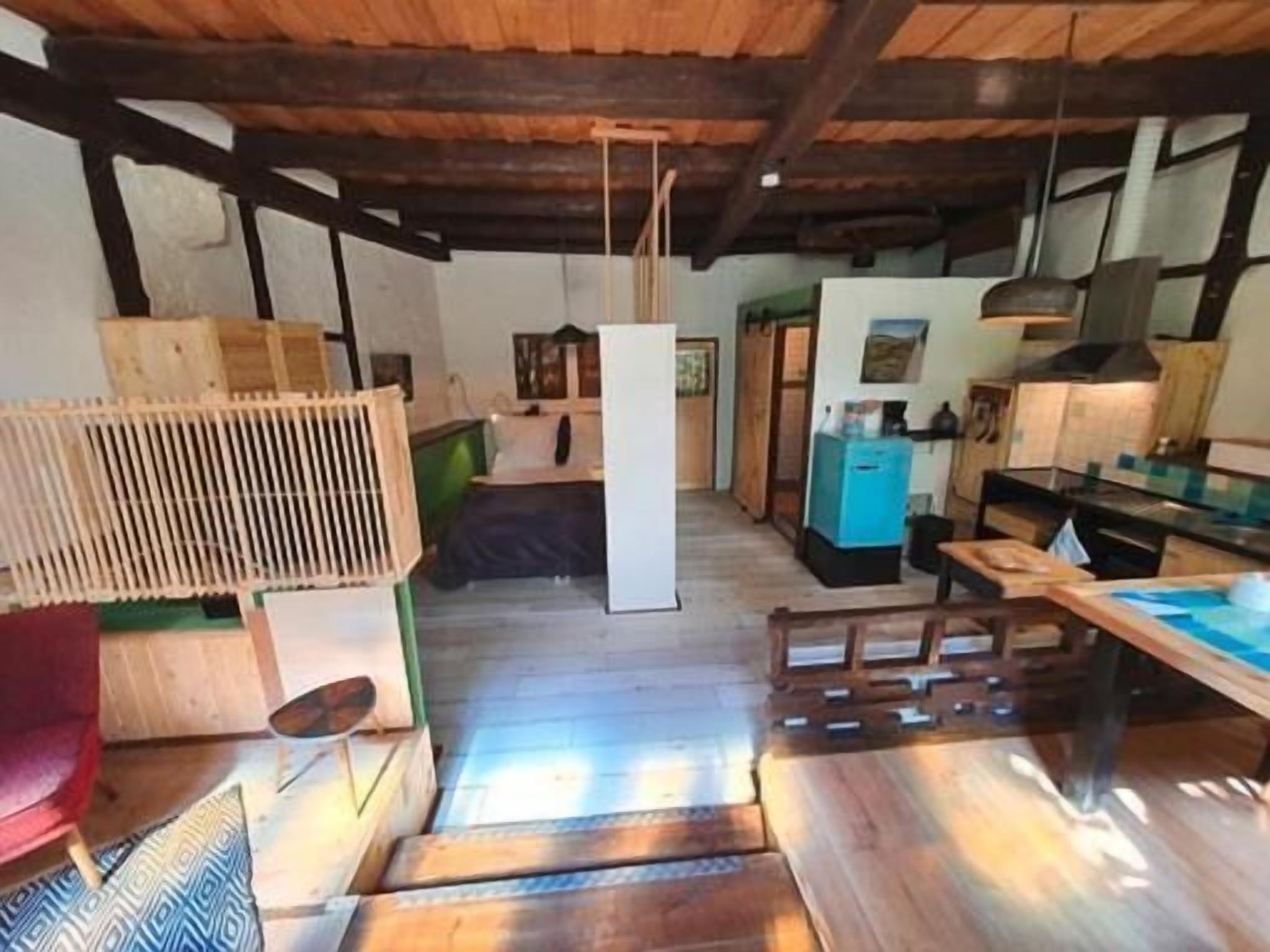 A rustic interior with exposed wooden beams, a kitchen area with a blue refrigerator, and a dining table with chairs.
