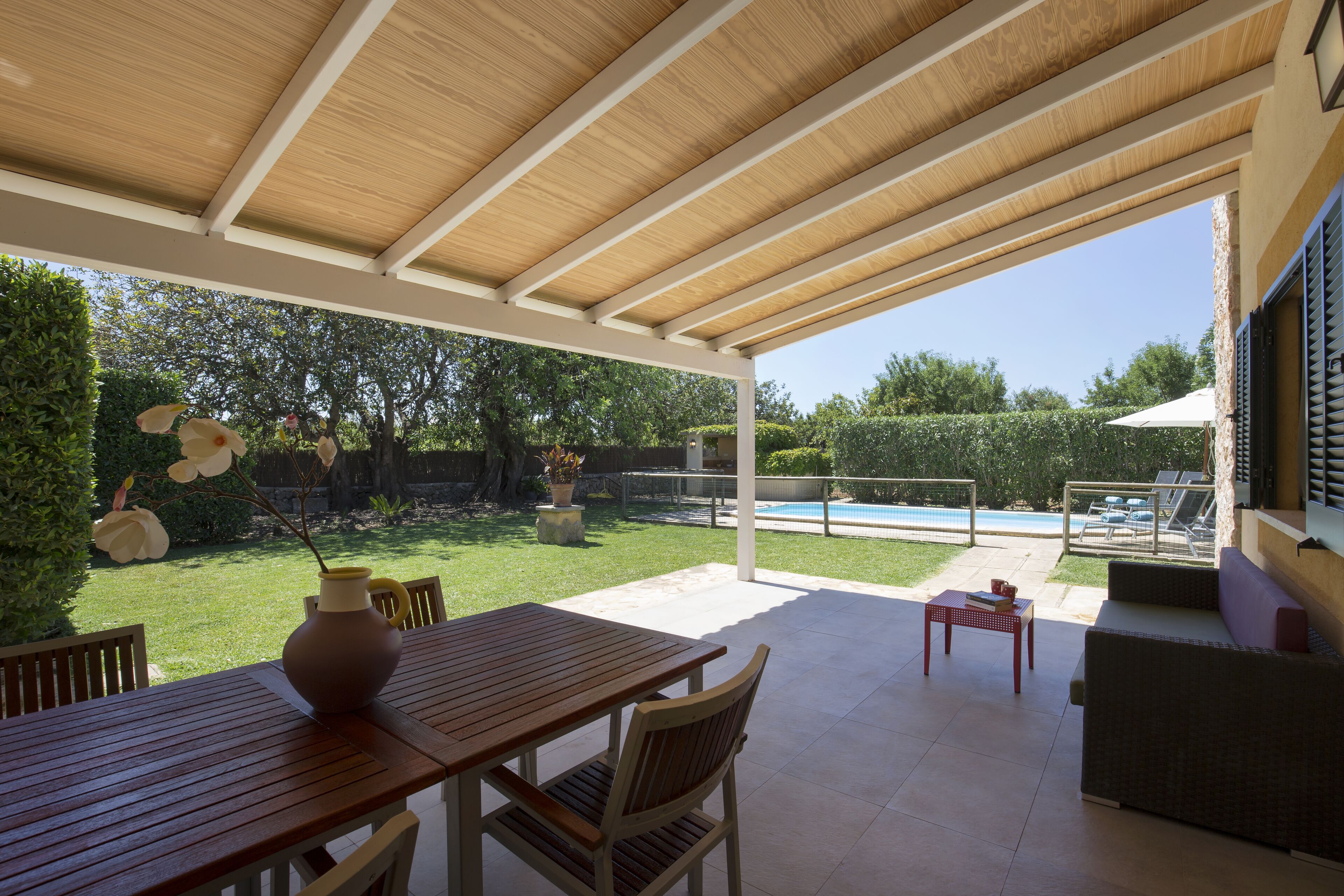 An outdoor patio with a wooden table and chairs, a small table, and a cushioned seating area.