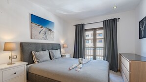 A neatly made bed with a towel, a bedside table with a lamp, a nightstand, and a large window with curtains. - Adeje paradise Duplex with sea view (adeje)