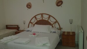 A neatly made bed with white linens and towels, a wooden headboard, bedside tables, and a small dresser. - Cozy Green Kitchen Apartment (marina di camerota)